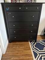 Full frontal image of IKEA Hemnes dresser showing six drawers with round knobs and several paint chips scattered on the surface and drawers.