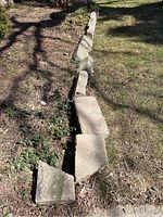 Outdoor garden border with large, heavy concrete or stone bricks arranged in a line along a garden bed edge. Bricks appear weathered with dirt and moss.