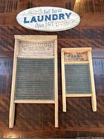 Photo showing two antique wooden washing boards with metal scrubbing ridges and a decorative laundry wall hanging mounted above them.