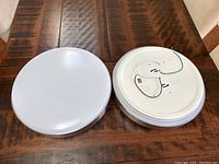 Two 16-inch round LED ceiling lights placed side by side on a wood table, showing white diffusers and metal backing with wiring.