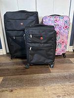 Three luggage pieces: two black Swiss Gear luggage and one floral Nine West luggage, all with 4 wheels. Smaller black Swiss Gear is carry-on size.