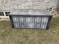 Front view of the outdoor storage box closed, showing wood panel design on black plastic exterior.