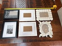 Top-down view of six assorted photo frames on wooden surface with measuring tape, showing arrangement and size approx 4x6 and 5x7.