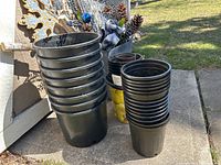 Stack of large, medium, and small black plastic pots on ground outside