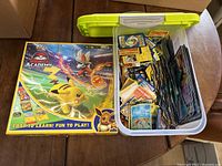 Pokémon Battle Academy board game box with a plastic bin of assorted Pokémon cards on a table.