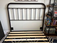 Photo of queen size metal bed frame headboard with vertical bars and metal frame sitting on a patterned carpet.
