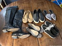 Full view of six pairs of shoes including boots, flats, and sneakers arranged on a wooden table.