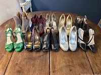 Photo showing 10 pairs of women's size 5 heels arranged on a wooden table including a variety of colors and styles: green, tan, red floral, yellow, black, white, and silver.