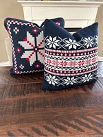 Two navy blue throw pillows with red and white snowflake designs on a wooden surface.