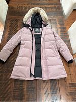 Front view of the TNA The Powder Parka laid flat on a wooden surface, showing exterior design with zip closure and faux fur trim on hood.