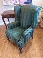Photo showing front side of green wingback chair with striped upholstery and wooden legs on hardwood floor.