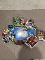 Photo showing assorted sealed board games including Scatter Brainz, Skylanders, Pirate's Plunder, and various small toy figures such as Star Wars Clone Trooper dog, Garfield figure, Snoopy figure, and plush dog.
