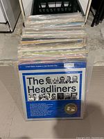 Stack of vinyl records with visible cover of The Headliners album including black and white portraits and blue background.