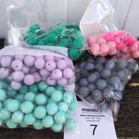 Bundles of sealed plastic bags containing silicone beads in various colors stacked together with a MaxSold auction sheet in the background.