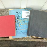 Three Charles Dickens books: a large black hardcover with embossed cover, a blue softcover A Christmas Carol book, and a small red hardcover Tale of Two Cities book.