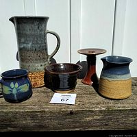 Five studio pottery pieces: large pitcher, small mug with floral design, taper candle holder, cream/dressing cup, and small brown bowl