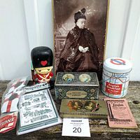 Full lot image showing all British themed items together on a wood surface against white background. Items include photograph, coin bank, tins, book, postcards and sunglasses.