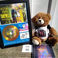 Photo showing the Elton John Farewell Yellow Brick Road limited edition collectors frame with protective sticker, the teddy bear with the tour shirt, and the Revamp CD.