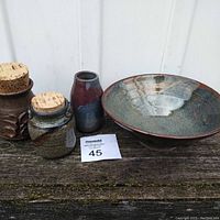 All four pottery pieces displayed together on a wooden surface: three small jars/vases (two with corks) and one bowl