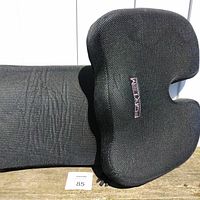 Pair of black memory foam cushions: one contoured lumbar support and one seat cushion, placed outdoors on wooden surface