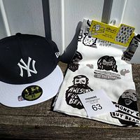 Front perspective photo showing New Era New York Yankees fitted hat next to BlueQ tea towel on a wooden surface in sunlight