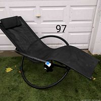 Side view of black orbital rocking lounge chair showing profile and mesh seating with pillow headrest.