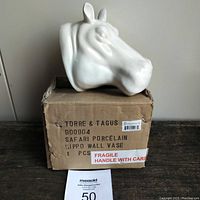 White ceramic hippo head wall vase sitting atop original cardboard box with printed label and fragile warning.