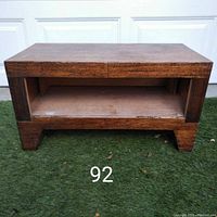 Front view of the wooden bench/table showing the rectangular open storage slot below the top surface and solid block-style legs.