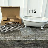 Photo showing the stainless steel stick-on soap dish with adhesive hooks and the small white ceramic bathtub soap dish, along with the opened product box.