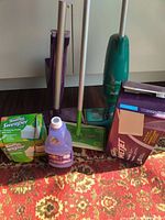 Overview photo showing all the cleaning tools and supplies including the Swiffer Sweeper, WetJet, vacuum, and various cleaning pads and cleaners.