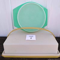 Rectangular cake carrier beige with yellow handle and green pie tray in background.