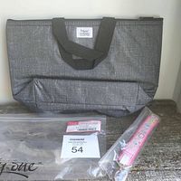Gray insulated lunch bag with black handles, front pocket, label showing 'Thirty One', and pink/white wrist keychain sealed in plastic.