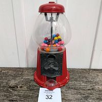 Front view of the gumball machine showing red metal base and top with clear glass globe containing multi-colored gumballs, coin mechanism, and a MaxSold tag.