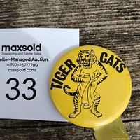 Front view of first yellow Tiger Cats button pin with tiger mascot and towel, black text