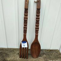Pair of large wooden tiki style fork and spoon showing full length and shape, placed outdoors on wood surface