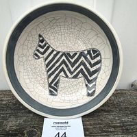 Full view of a round ceramic bowl featuring a zebra silhouette with black and white zigzag stripes against a cracked white glaze background and a grey rim.