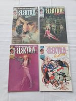 Four Elektra Assassin comic books displayed in plastic sleeves, showing front covers with different artwork featuring the main character and thematic elements.