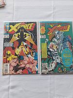 Two X-Force comics side-by-side showing front covers, one with a blue circular sticker for Marvel trading cards