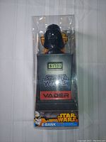 Front view of the unopened Star Wars Darth Vader E-Bank coin bank in retail box showing packaging design with LCD display and product branding.