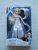 Front view of the Elsa doll packaged in original box showing white gown and musical feature badge