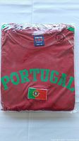 Photo of folded and packaged red Portugal soccer T-shirt size XL, with green Portugal text and flag patch, and Vestel brand tag.
