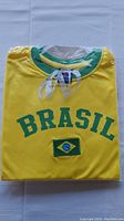 Photo of a brand new yellow Team Brazil soccer T-shirt folded with 'BRASIL' printed in green and Brazilian flag patch on the chest, size XL.