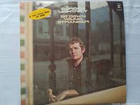 Front cover of Gordon Lightfoot's "Sit Down Young Stranger" vinyl album showing the artist in a seated pose with album title and sticker referring to the hit song 'If You Could Read My Mind'.