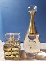 Photo shows full view of J'adore Dior perfume bottle and an embellished square perfume bottle.