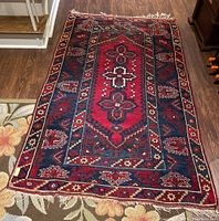 Full view of the machine made Asian style area rug showing red and blue geometric pattern and missing fringe on one short side.