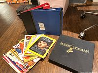 Photo showing two binders, a stack of magazines including National Geographic, and a large black Robert Bateman hardcover book.