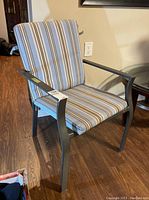 Front angle of one metal framed outdoor patio chair with striped cushion tied to frame, showing seat and backrest.