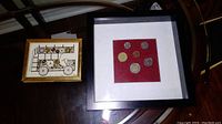 Framed Canadian coins contained in a black frame with red background seen on glass table.