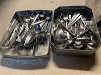 Two metal boxes filled with assorted flatware pieces including forks, spoons, and knives in various styles and sizes.