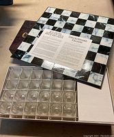 Top view of checkerboard game board inside box with clear glass shot glasses arranged in a tray.